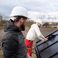 Two roofers fitting a standing-seam panel on a Sellwood re-roof